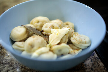 Traditional cooked pelmeni or dumplings in a blue bowl, seasoned with spices, bay leaf, and topped with melting butter for a hearty meal
