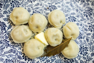 Close-up of freshly cooked pelmeni or dumplings served on a white and blue patterned plate, topped with butter and a bay leaf
