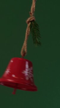A red Christmas bell with a winter ornament swings from side to side like a pendulum with a spruce branch on a rope.