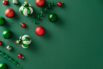 Christmas flat lay, top view. Red and green ornaments, curly ribbon, and confetti stars on a dark green background. Holiday background with copy space.
