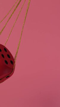 A red dice swings from side to side like a pendulum on a shiny gift rope against a pink background