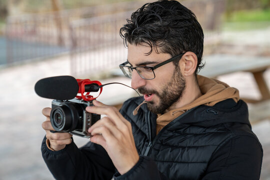 Male content creator filming video vlog with mirrorless camera and shotgun microphone setup outdoors - Powered by Adobe