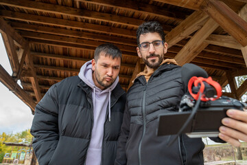 Vlogging creators live streaming together, two male friends recording online content outdoors with a professional camera