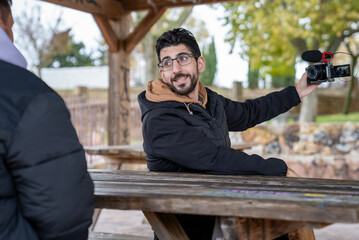 Fototapeta premium Content creator recording video with camera and microphone, interviewing person in outdoor park setting