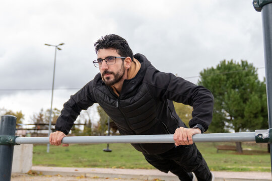 Man training outdoors at a park workout station, performing an inclined push-up for strength and physical fitness