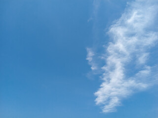 Soft white clouds stretch across a bright blue sky, creating a calm and airy atmosphere with abundant negative space ideal for text or design elements.