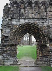 Naklejka premium Atmospheric landscape of St Andrews Abbey in Scotland, crumbling gothic architecture surrounded by a haunting graveyard beneath overcast coastal skies.