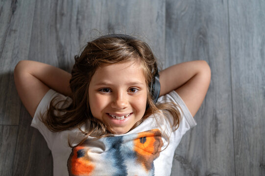 Smiling child girl lying on floor and listening music with headphones.