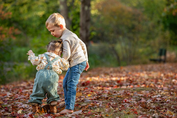 A brother helps his toddler sister walk in the park
