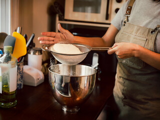 Woman sifting the flour into a metal bowl for making dough.