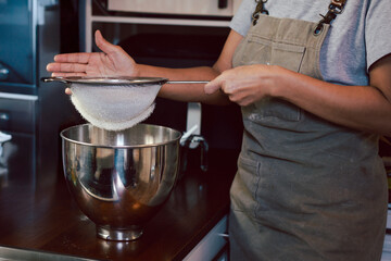 Woman sifting the flour into a metal bowl for making dough.