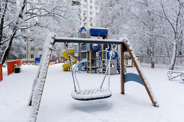Snowfall in the city. Children's swing covered with snow