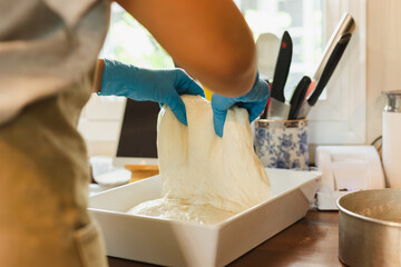 Woman hand with glove preparing bread dough on wooden table.