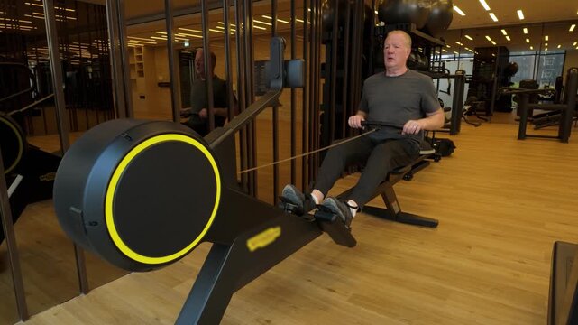 Close Up Shot Of A Senior Man Working Out On A Rowing Machine In A Indoor Gymnasium In Slow Motion.