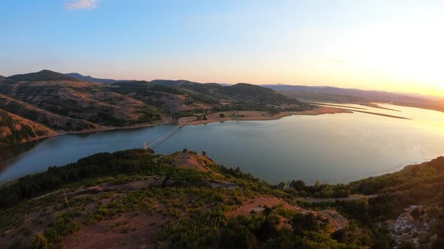 A sunset aerial over Studen Kladenets Reservoir in the Eastern Rhodopes, flying forward toward the Lisytsite suspension bridge &mdash; Bulgaria&rsquo;s longest hanging bridge. Warm light and dramatic scenic lands