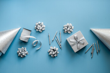 Festive party decoration in silver color with gift box and carnaval caps on blue background, top view