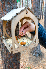 A man feeds the birds by placing food in a bird feeder.