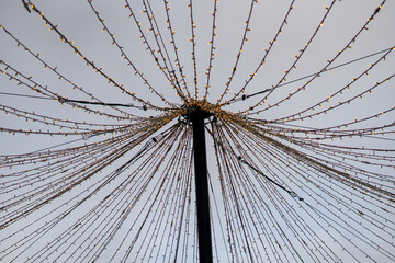 Radiating strings of festive lights hanging from a central pole against the sky as part of winter city decorations