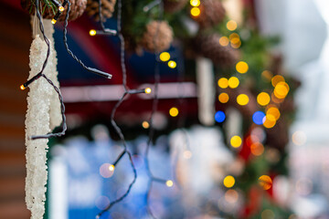 Close-up of artificial icicle and Christmas lights with bokeh background, pinecones, and festive greenery forming a warm holiday market decoration.