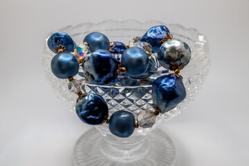 Macro defocused texture view of a translucent antique scallop edge footed lead crystal glass bowl, adorned with chunky blue color jewelry beads