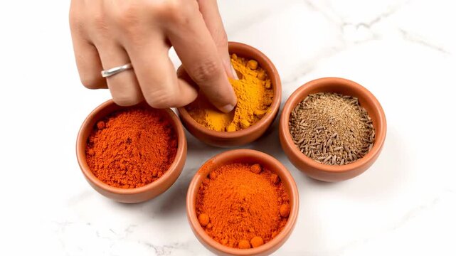 Womans Hand Selecting Aromatic Indian Spices from Clay Bowls.