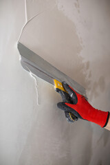 A masters hand in a red glove with a spatula does the work of leveling a wall with putty.