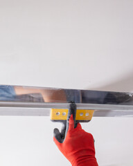 A masters hand in a red glove with a spatula does the work of leveling a wall with putty.