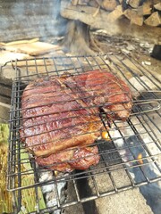 Rantau Panjang , Kelantan, Malaysia - November 18 2025: Close-up of a thick piece of meat grilling on a wire rack over a smoky, wood-burning outdoor fire pit.