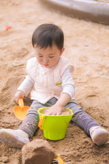 A toddler plays with sand, a green bowl, and an orange shovel outdoors.