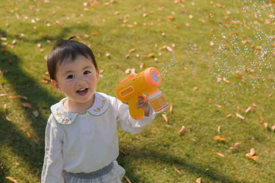 A child plays with a bubble blower, creating bubbles in an autumn park.