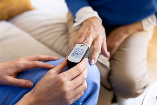 Nurse measuring oxygen saturation of senior woman with pulse oximeter at home