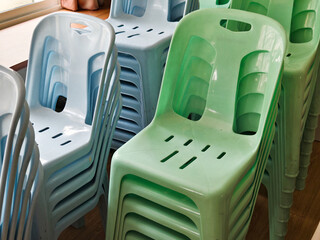 Stacks of pastel-colored plastic chairs arranged indoors, commonly used for community events, local gatherings, schools, or public halls. Simple everyday objects suitable for event or facility themes.