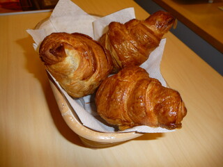 A basket of three freshly baked, golden, buttery croissants on a wooden table, ready to eat.