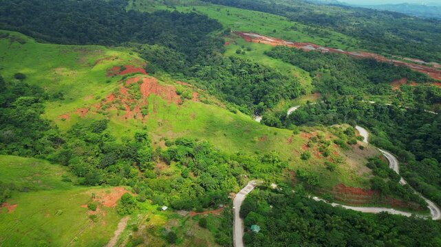 Downward aerial of Quinawan Mountain View in Mariveles, Bataan, highlighting rolling green hills and winding roads with scattered sunray spots illuminating the landscape.