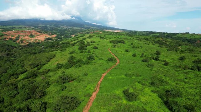 Closer elevated forward aerial showing a small trail winding through lush greenery and rolling hills, with scattered trees and exposed soil patches near Mariveles, Bataan.