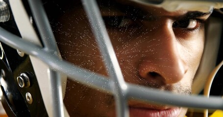 Staring adult football player peering through helmet facemask at sideline, with metal facemask bars