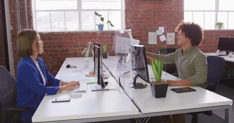 Typing Asian woman royal-blue-blazer, male light-green shirt placing sticky note at office divider