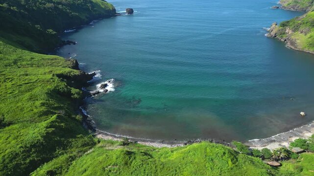 Tilt‑down aerial of Nagbayog View Deck in Mariveles, Bataan, revealing the curved coastline as lush green hills descend into turquoise waters under soft natural light.