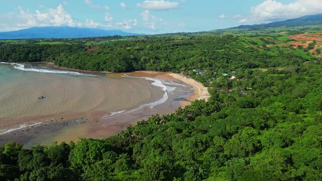 Circling aerial of Quinawan Beach in Mariveles, Bataan, highlighting brown water waves rolling toward the sandy coastline, framed by lush green forest and coastal hills.