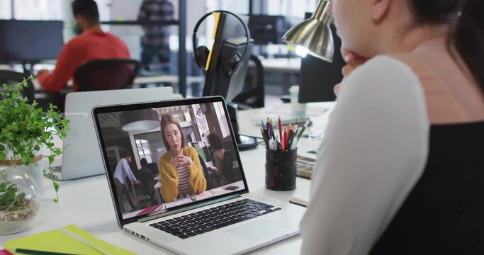 Watching woman in white long-sleeve top at open-plan desk with laptop and headphones, copy space - Powered by Adobe