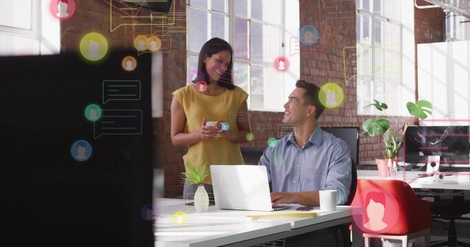 Talking coworkers wearing blue shirt, yellow blouse at open office using laptop, mug, chat overlay - Powered by Adobe