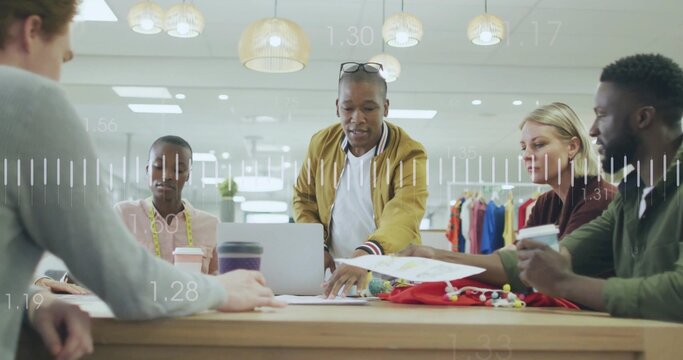 Leaning male team lead wearing mustard jacket pointing at laptop in studio, with fabric swatches - Powered by Adobe