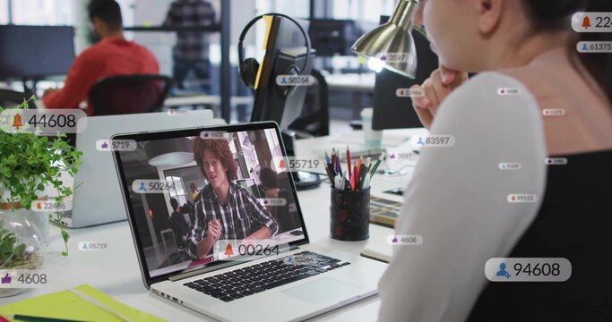 Watching female colleague viewing online call on laptop at open office, headset, badges, copy space