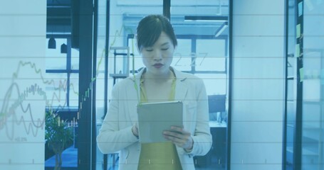Standing woman in pale blazer holding tablet at chest in modern office, displaying glass graphs