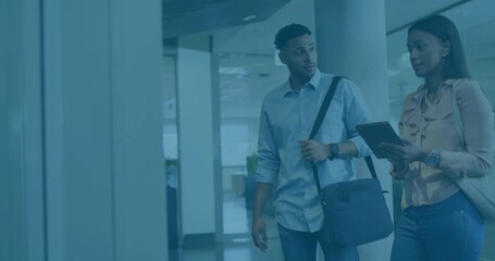 Walking coworkers consulting tablet in modern office, man in light blue shirt, woman in blouse