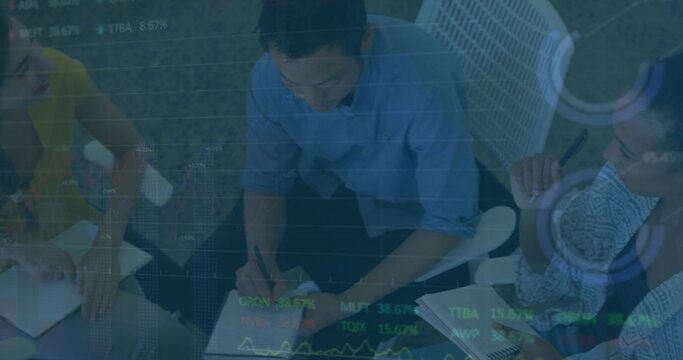 Discussing team leaning over pads, writing at round table, with yellow blouse and financial overlay