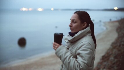 Adult woman drinking coffee by Baltic Sea at twilight in autumn - Powered by Adobe