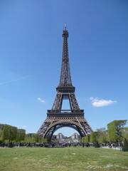 Fototapeta premium Stunning vertical view of the Eiffel Tower against a vibrant blue sky, captured on a clear summer day in Paris, France. This iconic landmark is framed by lush green lawns and distant trees