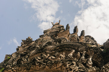 intricately carved, weathered stucco (or stone) reliefs adorning the gable or apex of an ancient temple structure, featuring mythological figures, layered sculptural details, and a central deity figur
