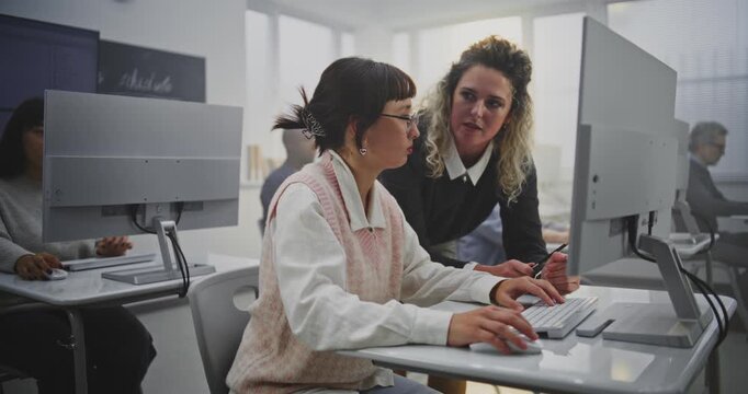 Professional Woman Educator Leads Programming Lesson For Adult Students. Teacher Stands Next Female Student, Checks Progress, Encourages Creative Problem Solving. Concept Modern Education, Motivation. - Powered by Adobe